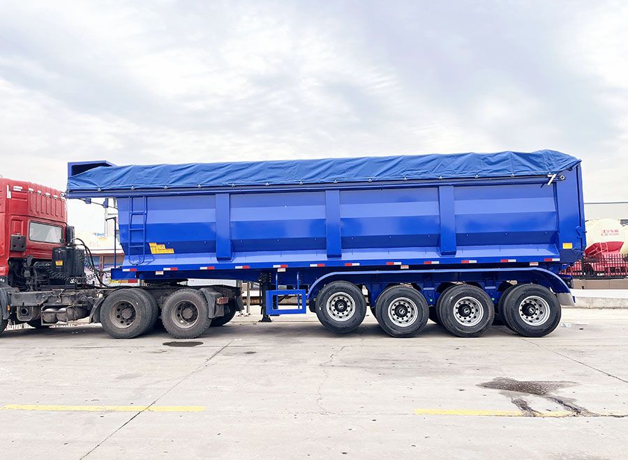 Blue four-axle rear dump trailer with a fitted blue cover