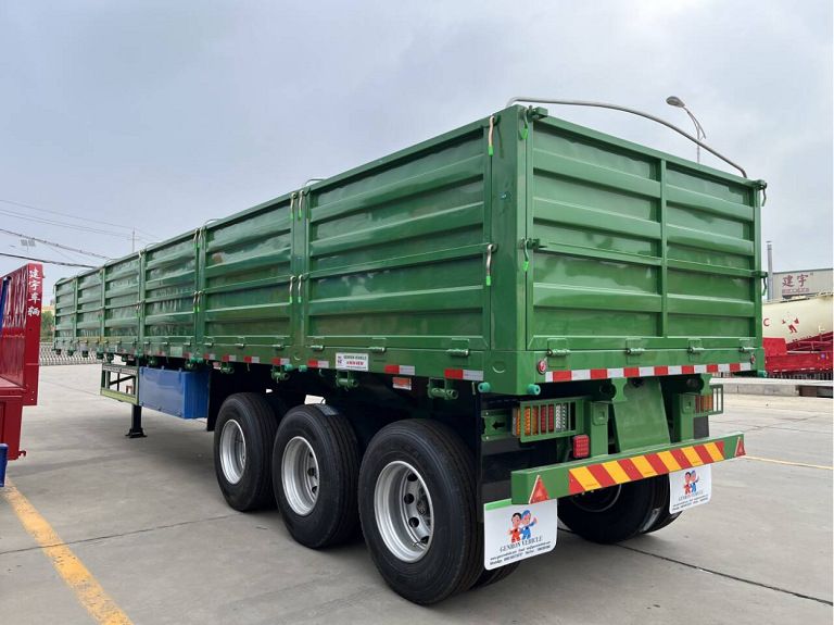 Green three-axle dropside semi trailer parked in the factory yard
